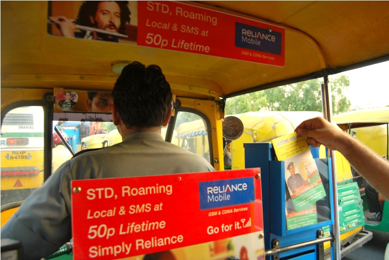 A driver driving auto that has branding of Reliance Mobile inside the auto rickshaw 
